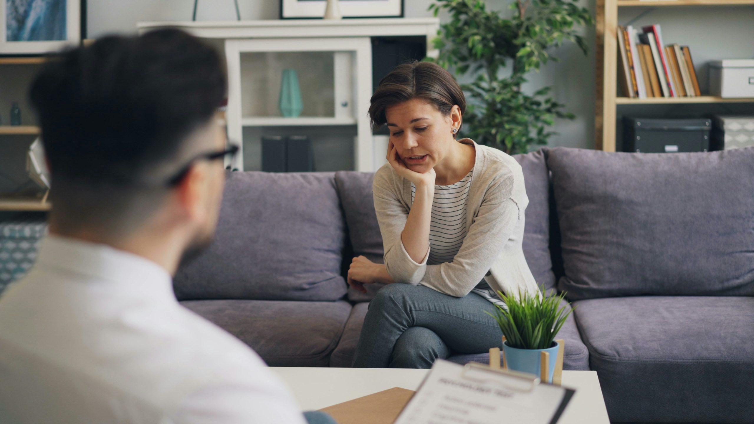 Vrouw in gesprek met adviseur aan tafel in huiselijke omgeving met paarse bank en kamerplanten