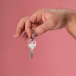 Hand holding a silver key with a pink background, symbolizing new home ownership.