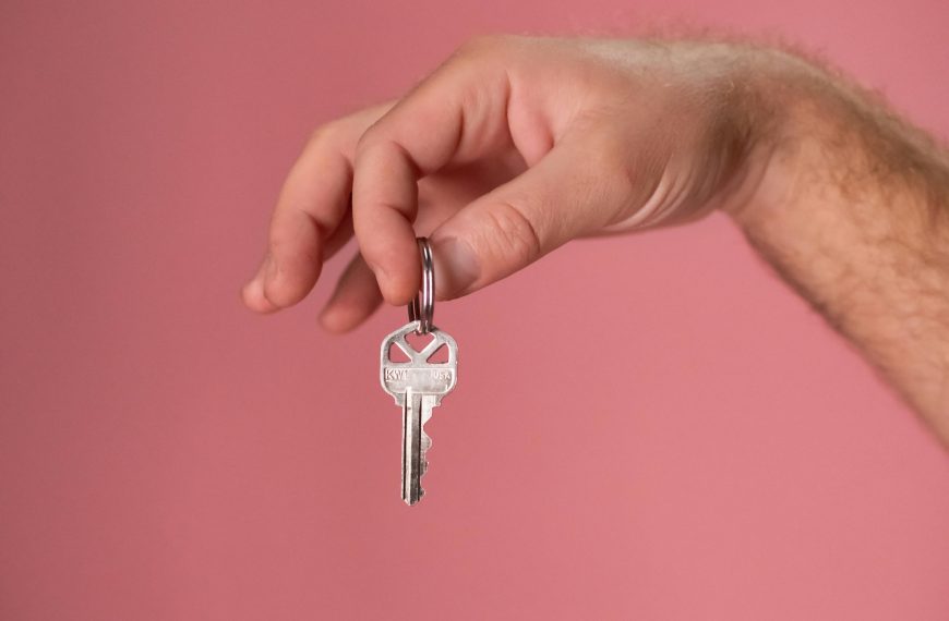 Hand holding a silver key with a pink background, symbolizing new home ownership.